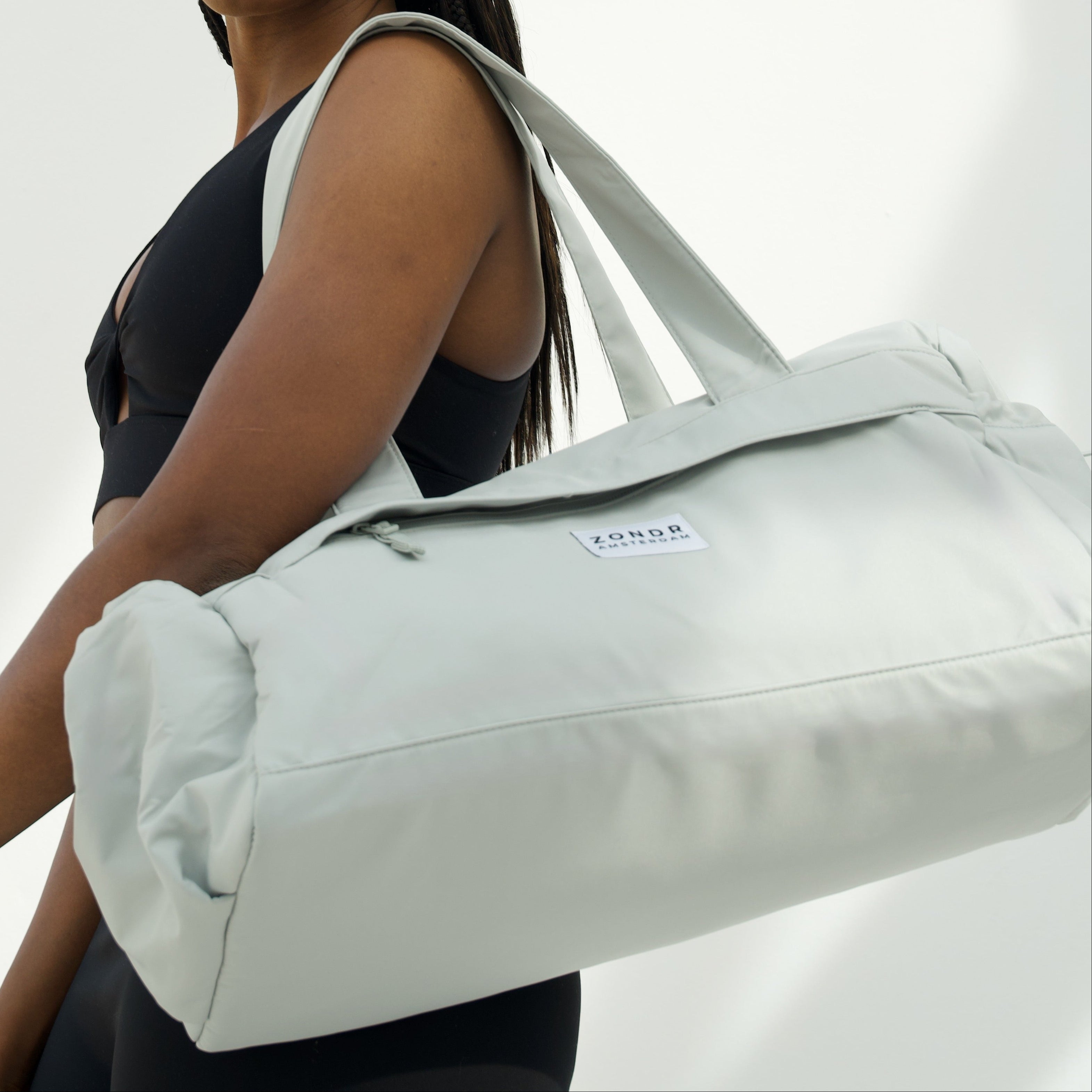Woman holding a light mint duffel bag against a white background